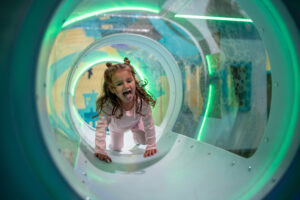 Tjej som räcker tungan klättrar genom en tunnel på ett lekland